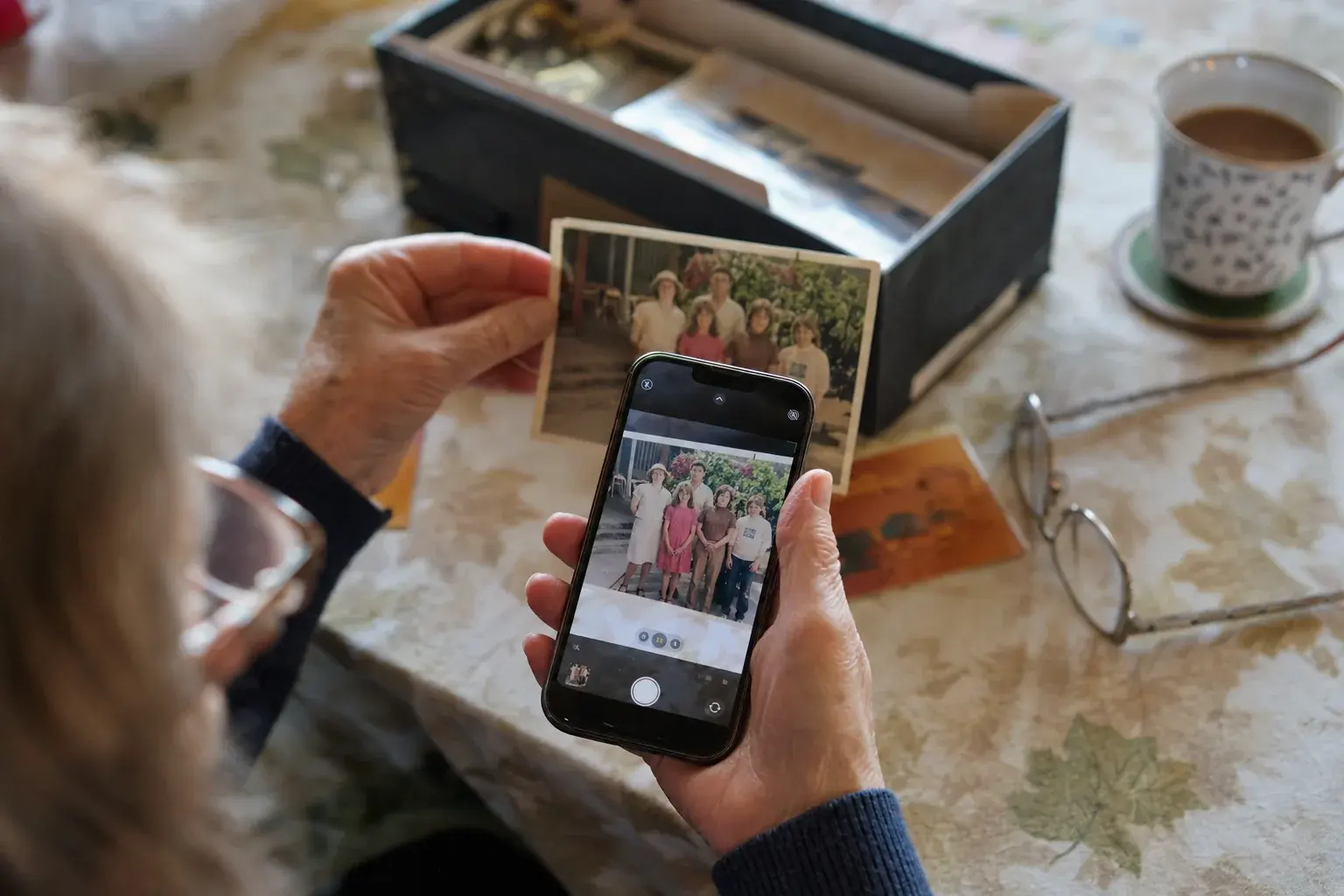 Weathered hands photographing an old family print with a phone